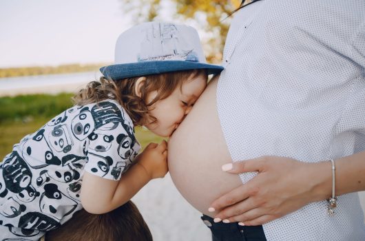 Pregnant mother Young and beautiful pregnant brunette in a white shirt on a beach with her little son